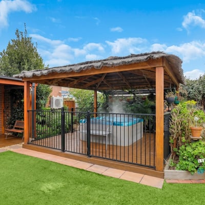 Discover a relaxing outdoor oasis featuring a covered patio and inviting hot tub surrounded by lush greenery.