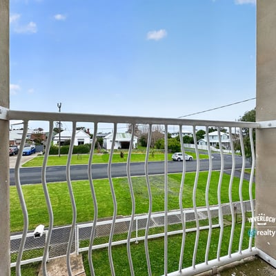 Enjoy a peaceful balcony view overlooking a quiet street surrounded by greenery and residential homes.