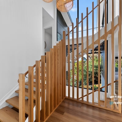 Modern staircase with striking wooden accents, leading to a bright, open living space filled with natural light.