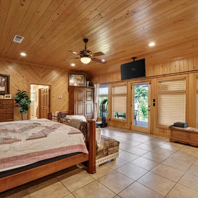 Spacious master bedroom featuring wood accents, large windows, and direct access to outdoor greenery.