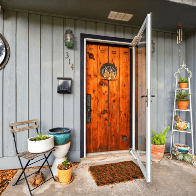 Inviting entryway featuring a striking wood door, potted plants, and a cozy seating area.