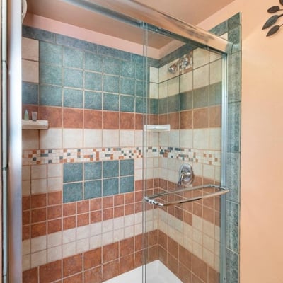 Bathroom shower featuring decorative tilework and glass doors, providing durability and easy maintenance within a rustic setting.