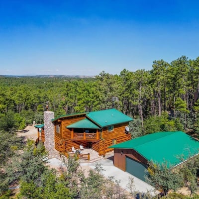 Aerial view showcasing the log home, detached garage, and surrounding trees. The durable metal roofing and natural materials reflect thoughtful design in this Prescott mountain setting.
