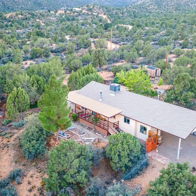 This elevated view highlights the wraparound deck, mature trees, and sprawling land. A serene retreat with endless possibilities for customization or self-sufficient living.