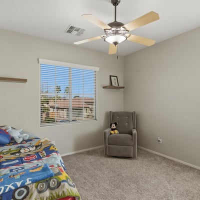 Bright bedroom with plush carpet, ceiling fan, and large window providing a welcoming space for family or guests.