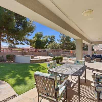 Shaded patio overlooking the landscaped yard and pool area, providing a comfortable outdoor living space for dining or relaxing.