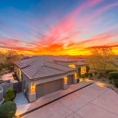 Beautifully maintained Scottsdale home with modern architecture, spacious driveway, and warm exterior lighting set against a vibrant sunset backdrop.