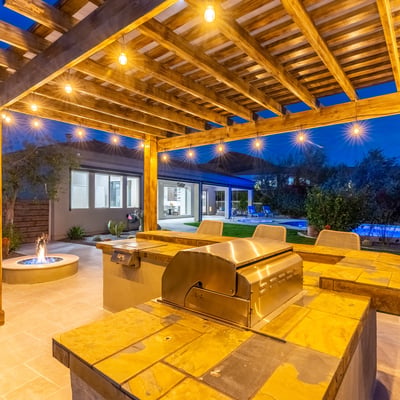 Scottsdale pergola kitchen with built-in grill, bar seating, and warm lighting, ideal for entertaining after sunset.
