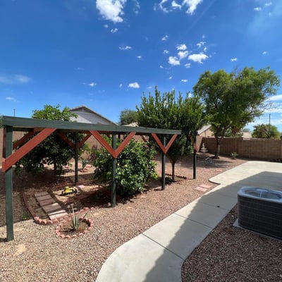 Spacious backyard with mature trees, low-maintenance desert landscaping, and a charming shaded garden structure. An inviting outdoor setting with room to enjoy and personalize.
