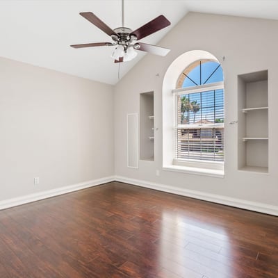 Soaring vaulted ceilings, decorative wall niches, wood flooring, and an elegant arched window create a bright and welcoming bedroom filled with natural light.