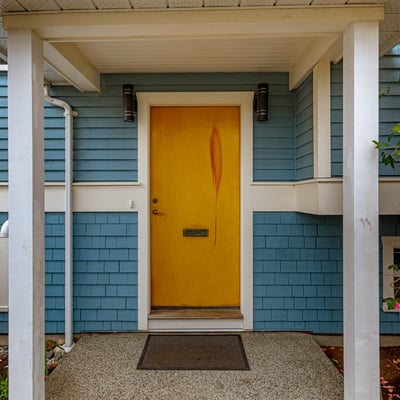 Bright yellow door welcomes you to this inviting home, framed by lush greenery and vibrant blooms.
