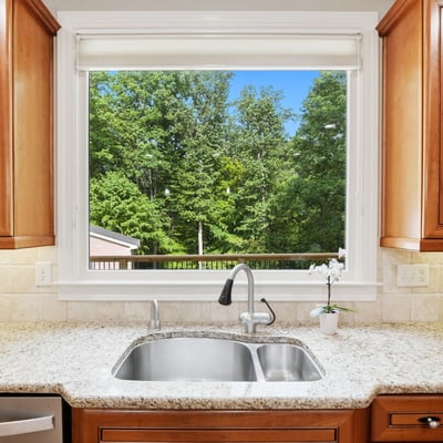 Bright kitchen featuring rich wood cabinetry and a scenic view of lush greenery through a large window.