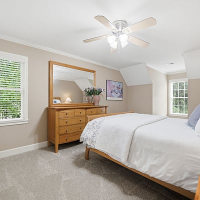 Bright and airy bedroom featuring natural light, modern ceiling fan, and ample storage in a cozy setting.