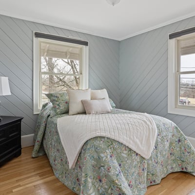 This inviting bedroom features cozy decor, ample natural light, and a tranquil view from the windows.