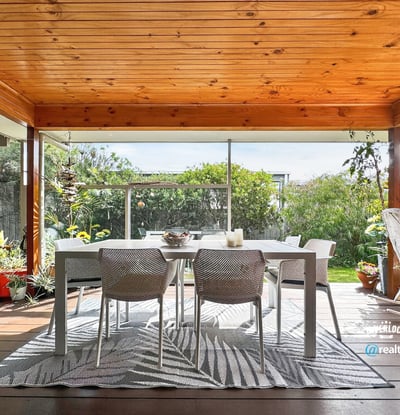 Spacious covered patio surrounded by lush greenery, perfect for outdoor dining and relaxation.