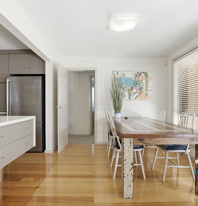 Bright and airy dining space featuring a rustic wooden table, modern kitchen amenities, and abundant natural light.