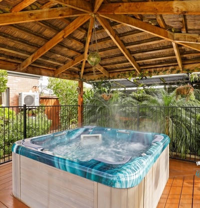 Relax in this private hot tub surrounded by lush landscaping under a rustic wooden pergola.