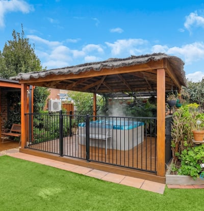 Discover a relaxing outdoor oasis featuring a covered patio and inviting hot tub surrounded by lush greenery.