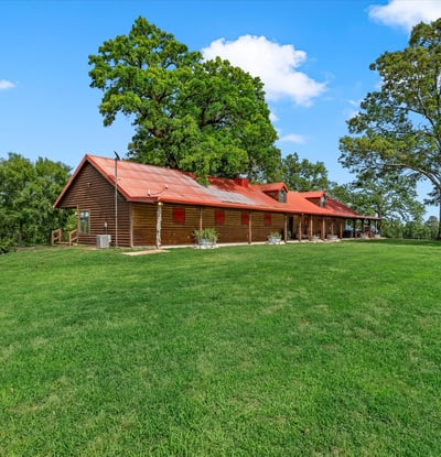 Spacious countryside home with a welcoming porch, surrounded by lush greenery and open skies.