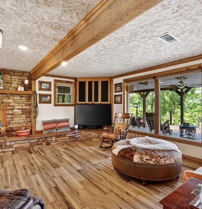 Spacious living area features wood accents and large windows overlooking a picturesque outdoor landscape.