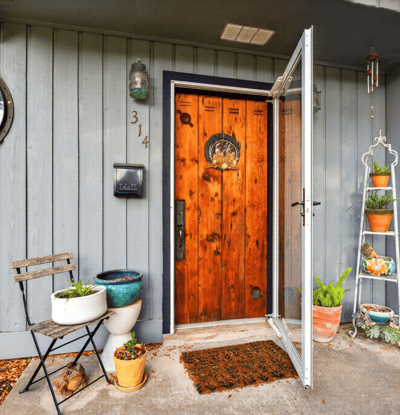 Inviting entryway featuring a striking wood door, potted plants, and a cozy seating area.