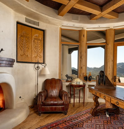 A custom kiva-style fireplace anchors this intimate office, surrounded by artisanal finishes and panoramic desert views. This thoughtfully curated space offers sophistication and warmth for working or relaxing in style.