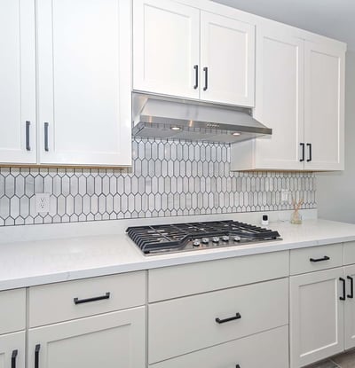 A stunning combo of form and function with a built-in gas cooktop, vertical tile backsplash, and crisp white cabinetry designed for serious home chefs.