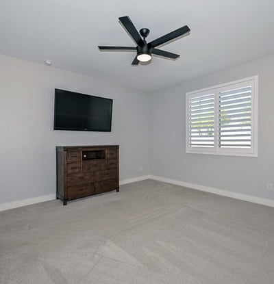 A peaceful primary suite with soft gray tones, upgraded ceiling fan, and bright natural light designed for restful living in this Peoria home.