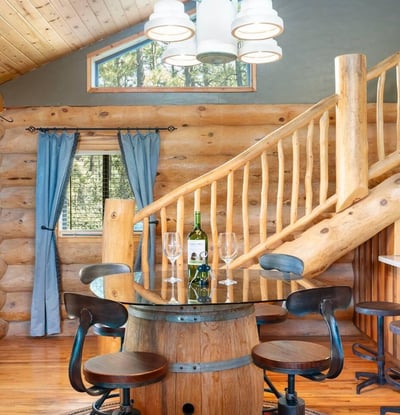 Dining area with handcrafted barrel table, log staircase, and warm wood finishes that reflect the home s authentic Prescott log construction.