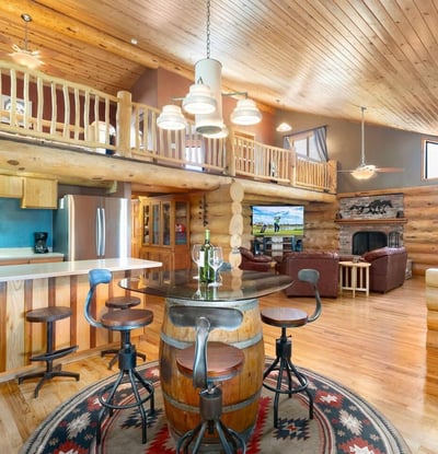 Open-concept great room showcasing vaulted ceilings, loft overlook, dining area, and stone fireplace all anchored by rich wood textures.
