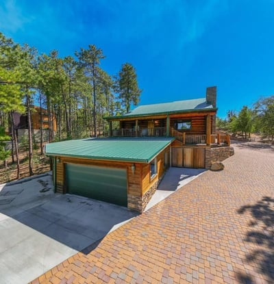 Wide paver driveway leading to a detached garage and covered entry. The stone chimney, metal roof, and wood exterior showcase craftsmanship and durability suited for Prescott s climate.