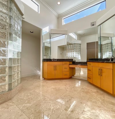 Spacious bathroom with high ceilings, glass-block shower, and granite vanities. Elegant design and natural light define this luxurious space.