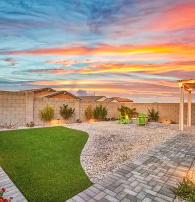 This wide-angle twilight photo highlights the home s large backyard with modern landscaping, upgraded paver paths, and a welcoming fire pit lounge in Litchfield Park.