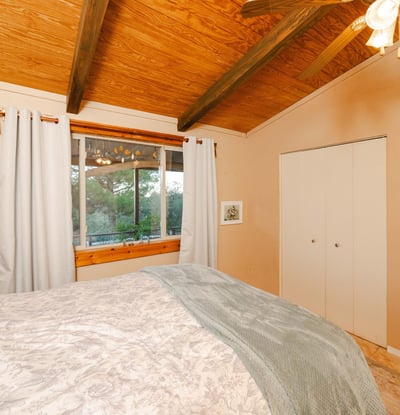 This inviting guest bedroom features vaulted ceilings and a large window that frames lush desert scenery. A comfortable retreat for visitors in a calm Hackberry setting.