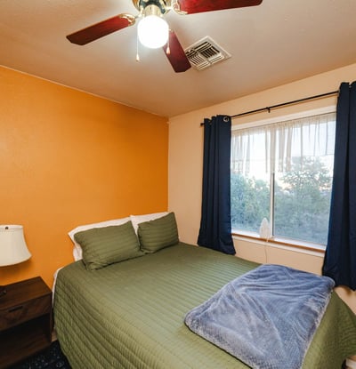 A cozy bedroom space offering soft lighting, ceiling fan, and window views of the natural desert surroundings. Ideal for guests or flexible use in this tranquil Hackberry home.