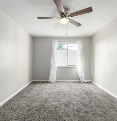 Spacious primary suite featuring plush carpeting, modern ceiling fan, and natural light perfect for rest and comfort in this Phoenix property.