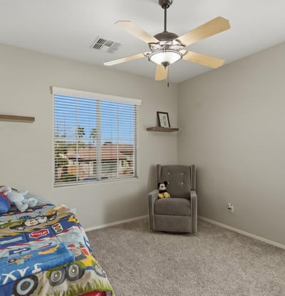 Bright bedroom with plush carpet, ceiling fan, and large window providing a welcoming space for family or guests.