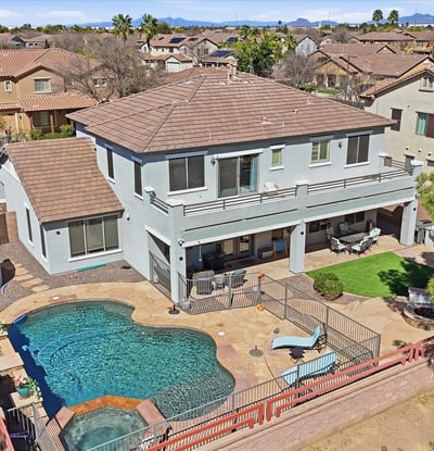 Drone perspective highlighting the backyard retreat with pool, spa, covered patio seating, and landscaped outdoor entertaining areas.