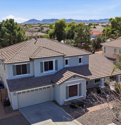 Elevated drone view showing the home's position within the neighborhood with distant mountain scenery and surrounding residential streets in Queen Creek.