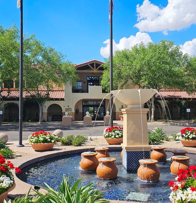 Clubhouse and fountain area surrounded by lush landscaping and mature trees. This Phoenix golf community offers a resort-style atmosphere and amenities.