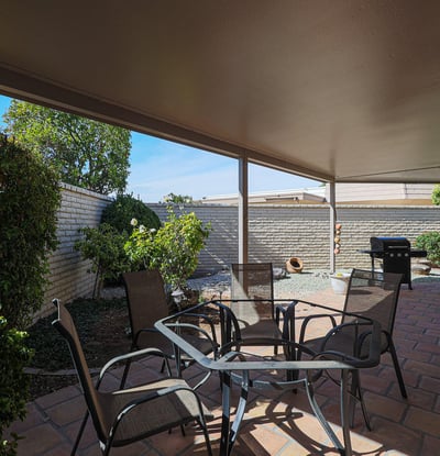 Private covered patio with mature landscaping and seating space, perfect for relaxing or hosting guests outdoors.