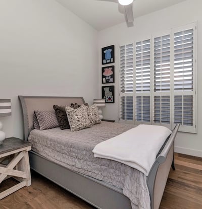 Bright guest bedroom with plantation shutters, wood floors, and neutral finishes, offering a relaxing space in this Phoenix home.
