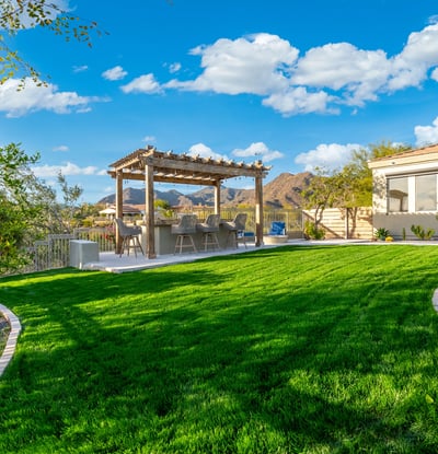 Scottsdale backyard with green lawn, pergola-covered kitchen, and scenic mountain backdrop, perfect for entertaining.