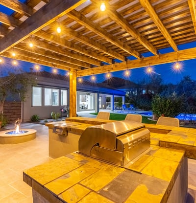 Scottsdale pergola kitchen with built-in grill, bar seating, and warm lighting, ideal for entertaining after sunset.