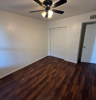 Comfortable bedroom featuring a ceiling fan, large closet, and attractive wood-look flooring. The spacious layout provides flexibility for bedroom furnishings while maintaining a bright and inviting atmosphere.