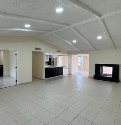 Open living room with dramatic wood-beamed ceilings, tile flooring, and a statement fireplace. The spacious design offers flexibility for entertaining and comfortable daily living.