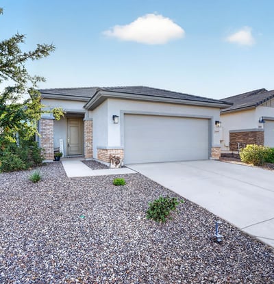 The welcoming front entry is complemented by attractive desert landscaping, mature greenery, stone accents, and a spacious driveway, creating a polished first impression of this Surprise property.