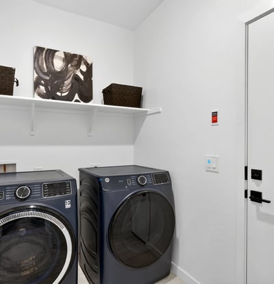 Designed for convenience, this laundry room includes upper shelving, modern appliances, and direct garage access to simplify everyday routines while maximizing storage.