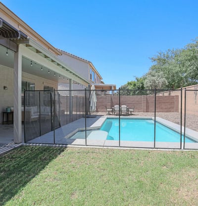 Spacious backyard featuring a fenced pool, covered patio, and open green space ideal for recreation and outdoor enjoyment. A well-designed backyard retreat in desirable Waddell.