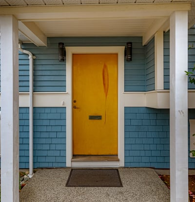 Bright yellow door welcomes you to this inviting home, framed by lush greenery and vibrant blooms.